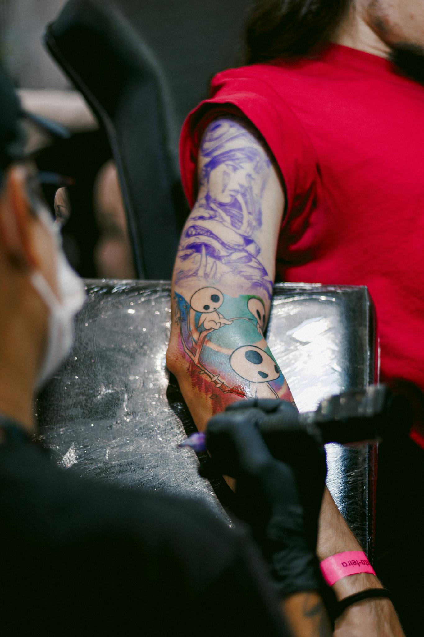Tattoo artist creating a vibrant sleeve tattoo on a client's arm in a modern studio.