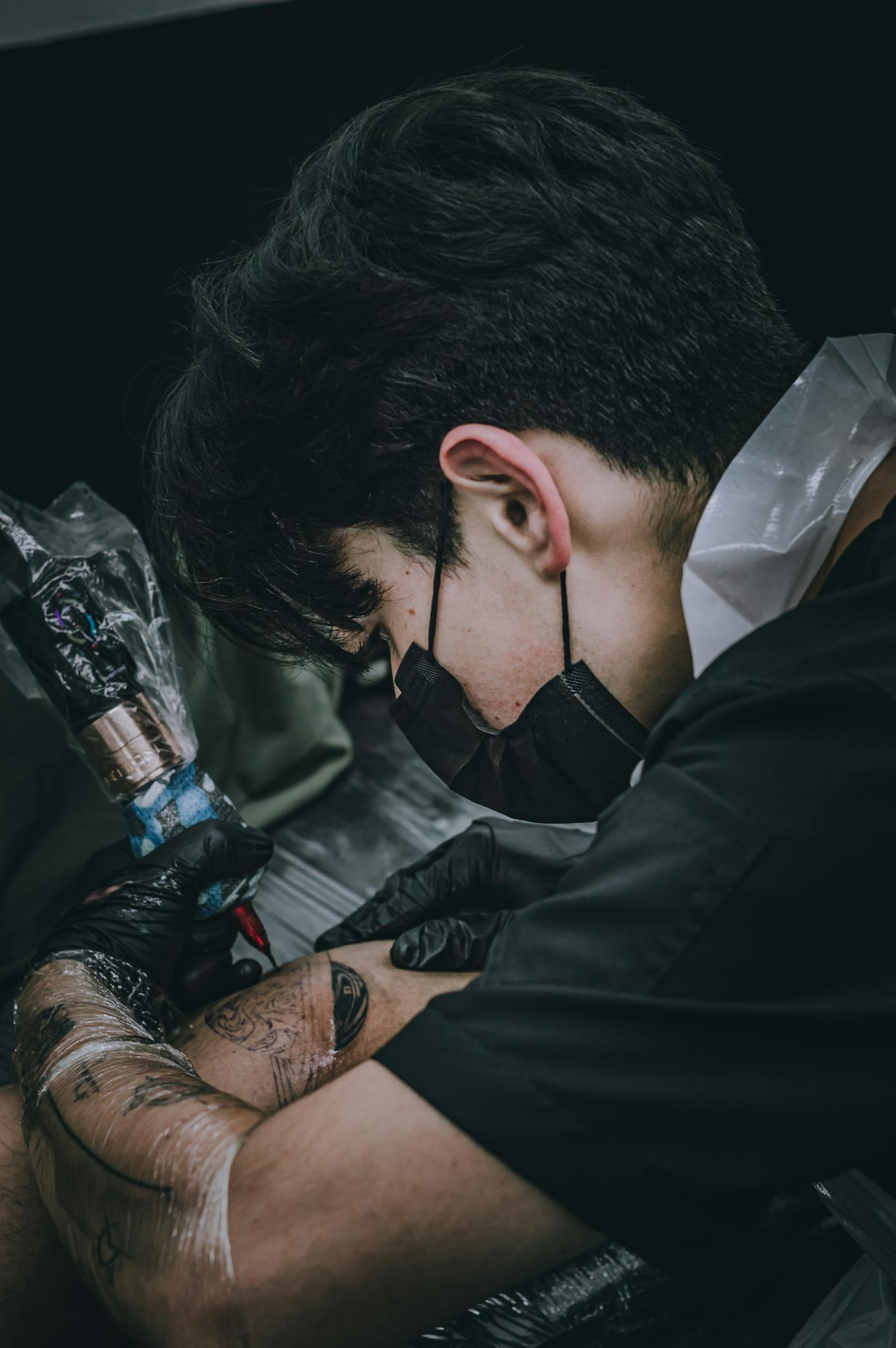 Tattoo artist focused on creating a detailed design in a Bogotá studio. Dark and artistic tone.
